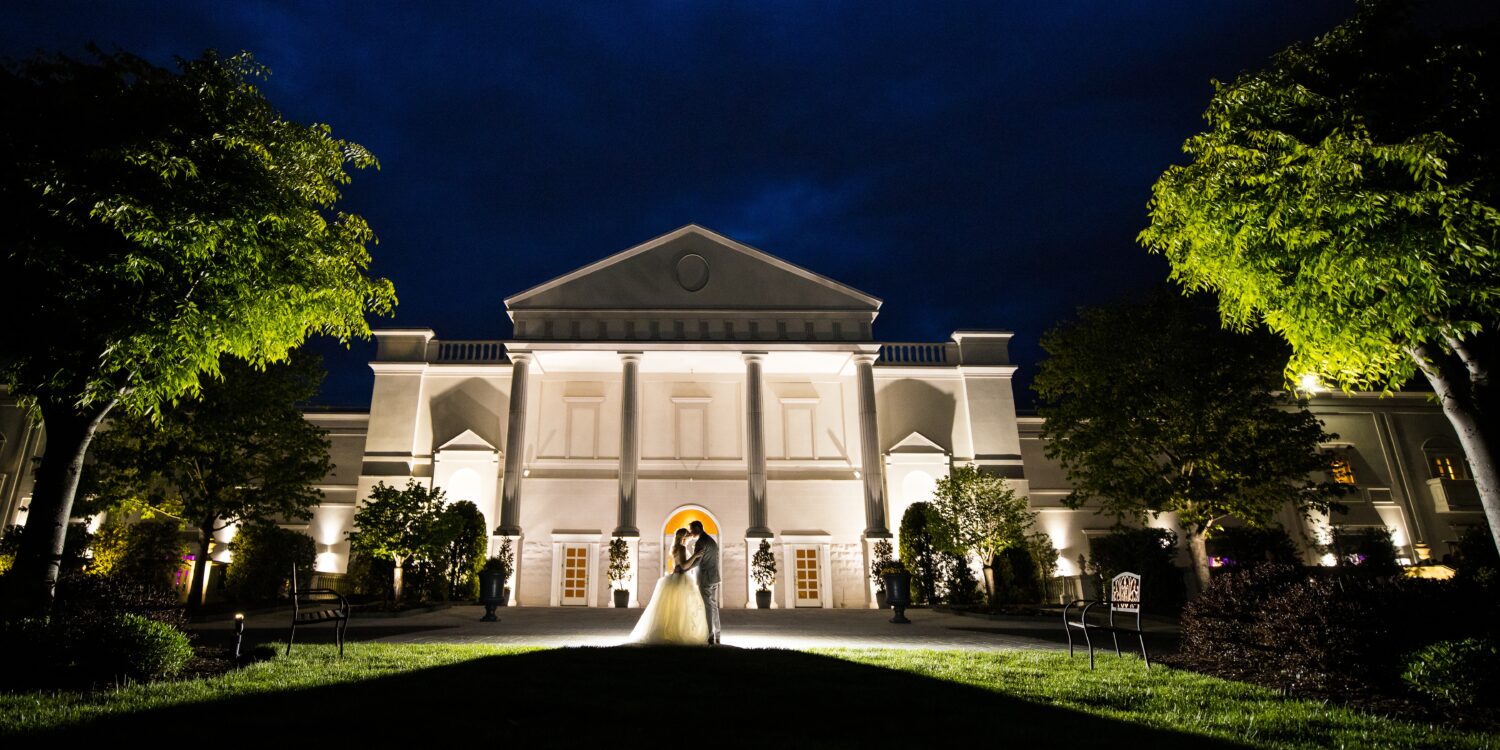 stunning night time portrait of the bride and groom as they stand together in front of their venue in New Jersey 