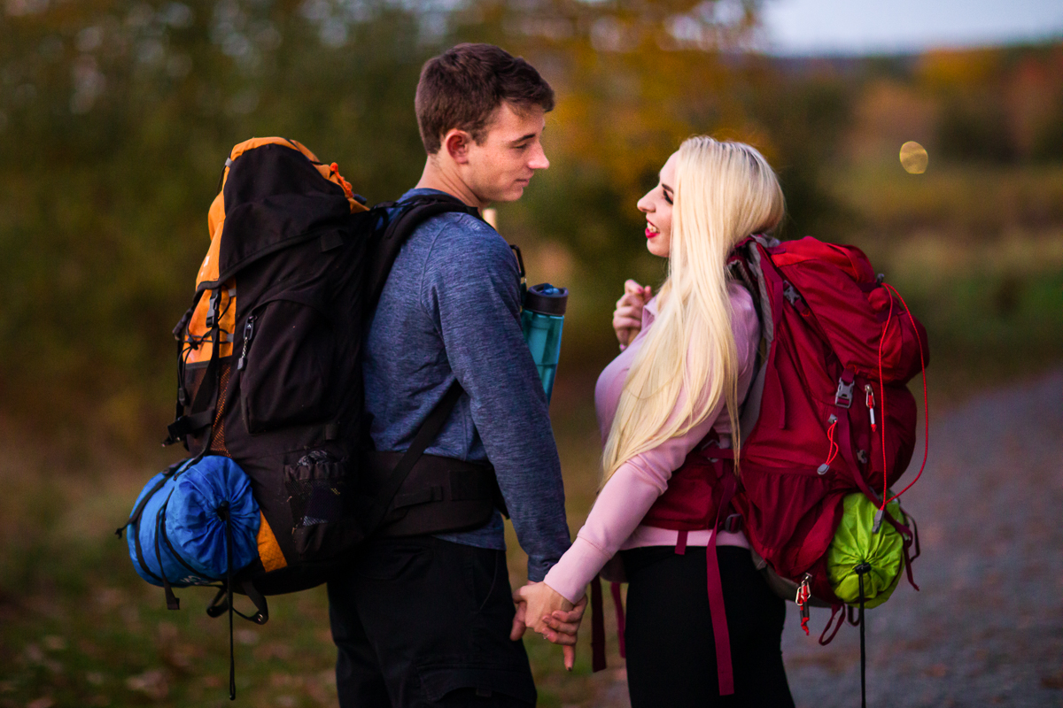 pennsylvania engaged couple holding hands while hiking in the autumn forest wearing back packs