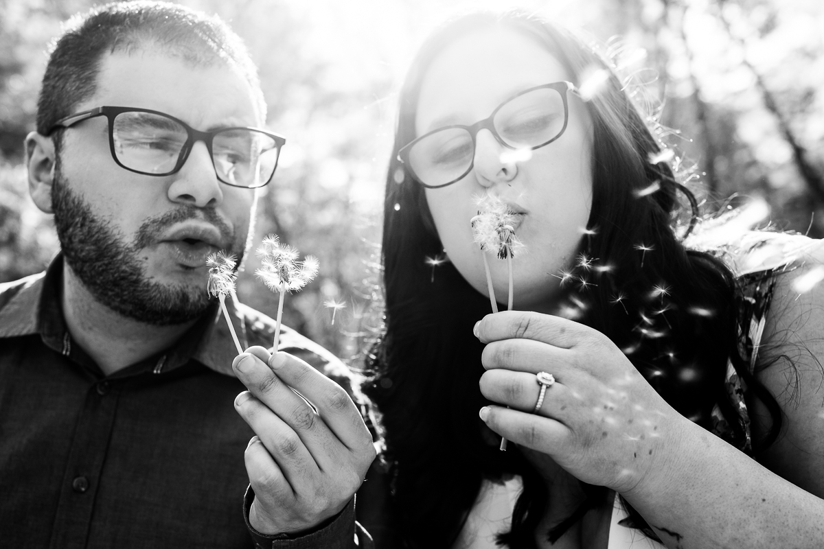 black and white photo of couple wearing glasses blowing dandelion seeds