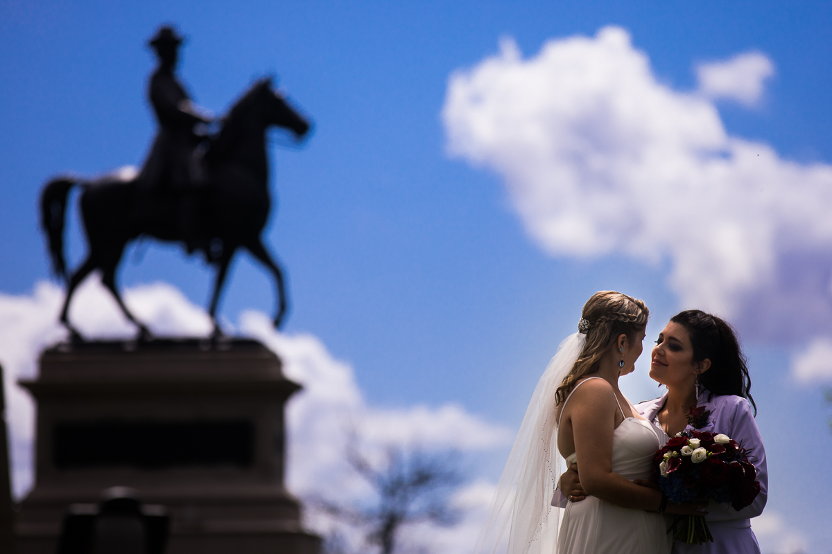 two brides look at each other with Gettysburg Pennsylvania horse statue bright blue sky background