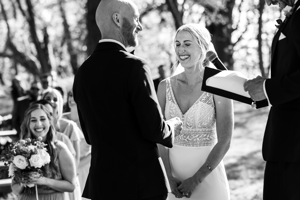 bride and groom at outdoor altar with officiant in black and white with guests in background