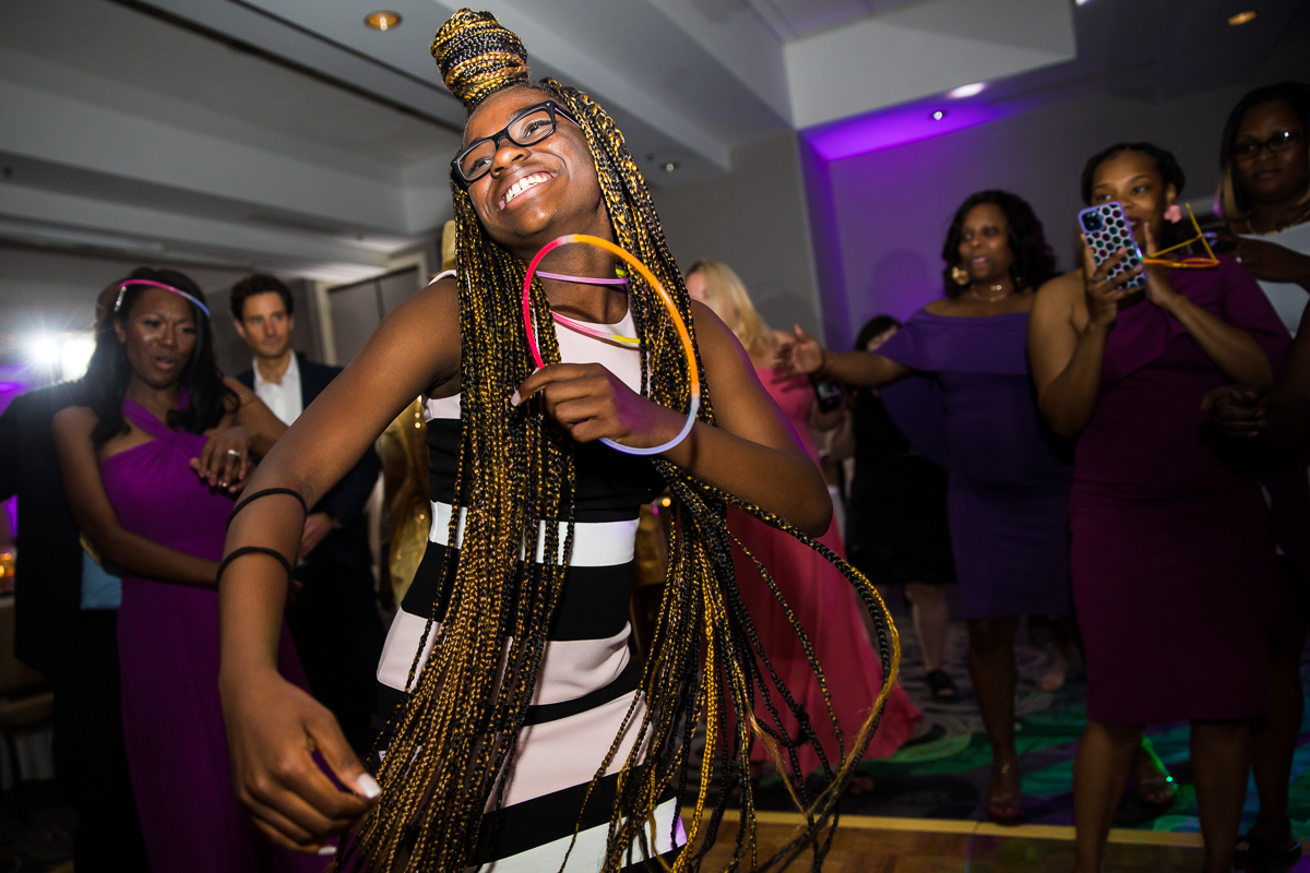 girl with braids holding glowstick necklace dances and smiles during wedding reception