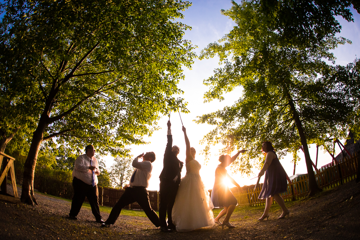 harry potter themed wedding vibrant outdoor wedding party photos at mount hope estate trees in background bride and groom pointing wands at sky with wedding party in background
