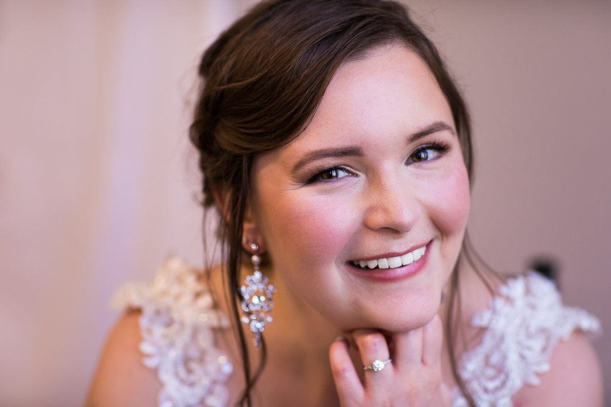 traditional bridal portrait of bride smiling and looking at camera with round wedding ring and dangling earrings