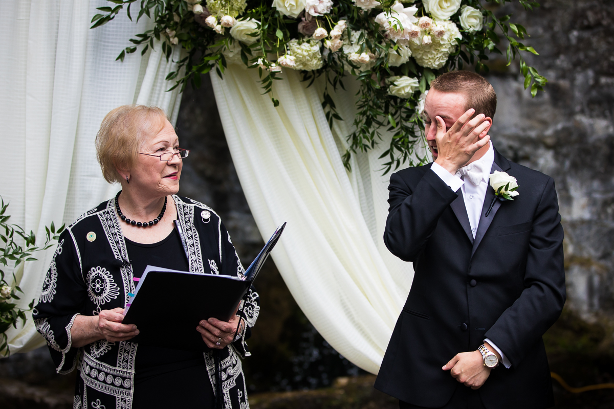 officiant and groom wiping tears from his eyes at the front of the altar during wedding ceremony