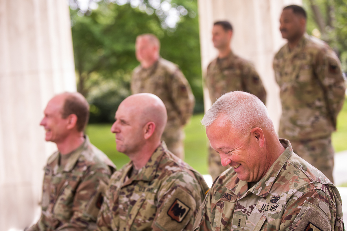 army men sitting during promotion ceremony smiling wearing camouflage uniform