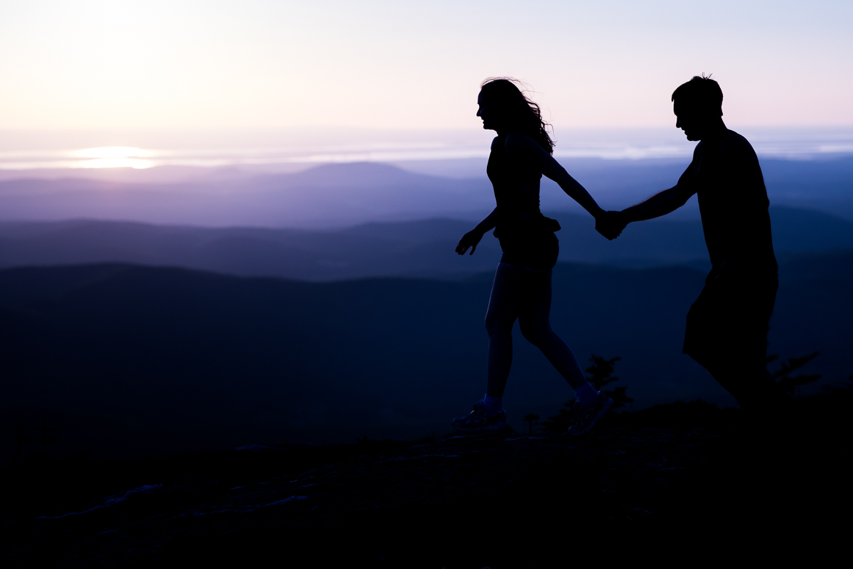 couple walking silhouetted against blue and purple ombre twilight background on top of mountain best award winning outdoor lifestyle photographer on east coast