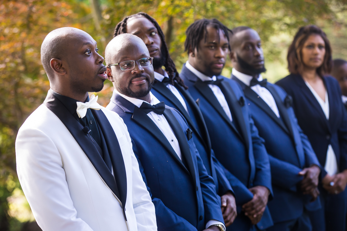 groom reacting to seeing bride walking down the aisle while groomsmen stand next to him wearing blue suits