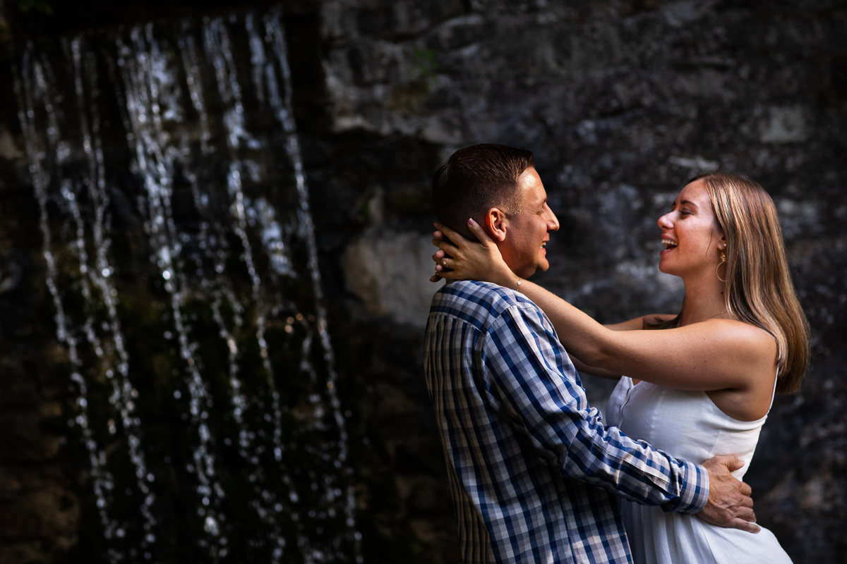 omni Bedford Springs resort engagement photographer couple standing in front of waterfall smiling at each other 