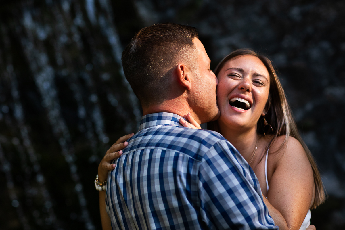 authentic emotional candid real natural wedding photographer fiancé kissing girl on cheek while girl laughs and smiles in front of waterfall omni resort