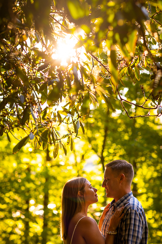 best award winning central pa engagement and wedding photographer couple looking at each other with sun peaking behind trees in middle of forest