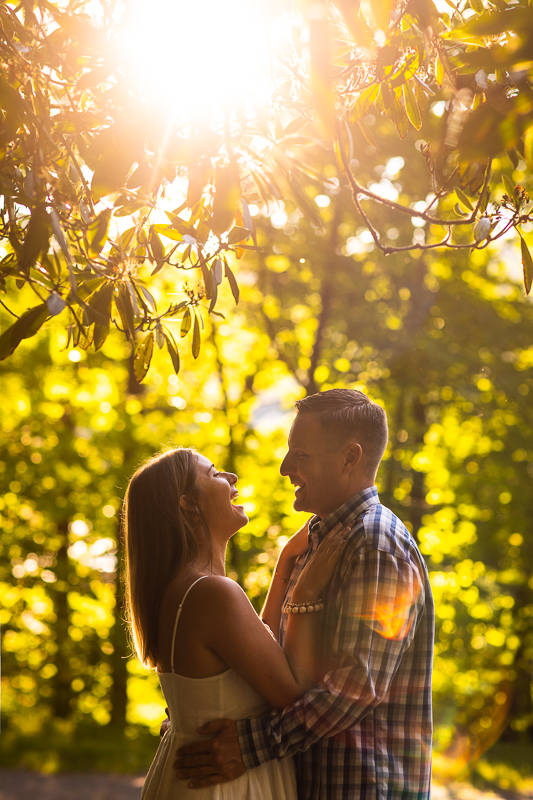 vibrant authentic creative wedding photographer couple wearing white dress and plaid shirt laughing with each other with arms around each other solar flare surrounded by forest