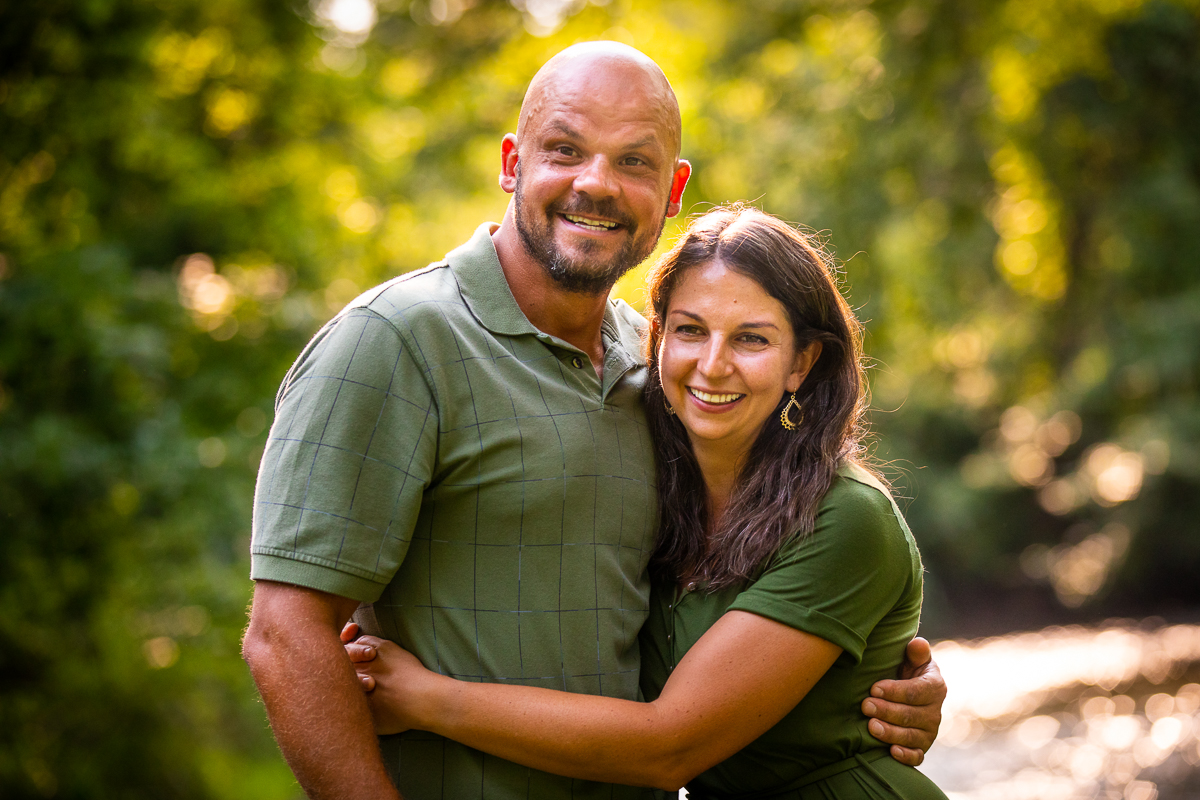 best family photographer husband and wife outside surrounded by trees smiling at camera wearing green