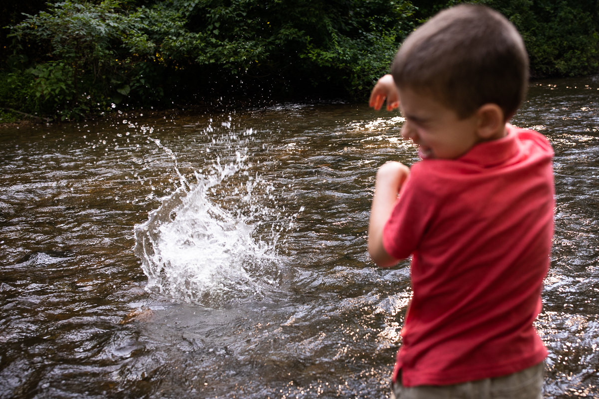best candid outdoor lifestyle photographer kid throwing stone into water at yellow breeches wearing red shirt rock splashes