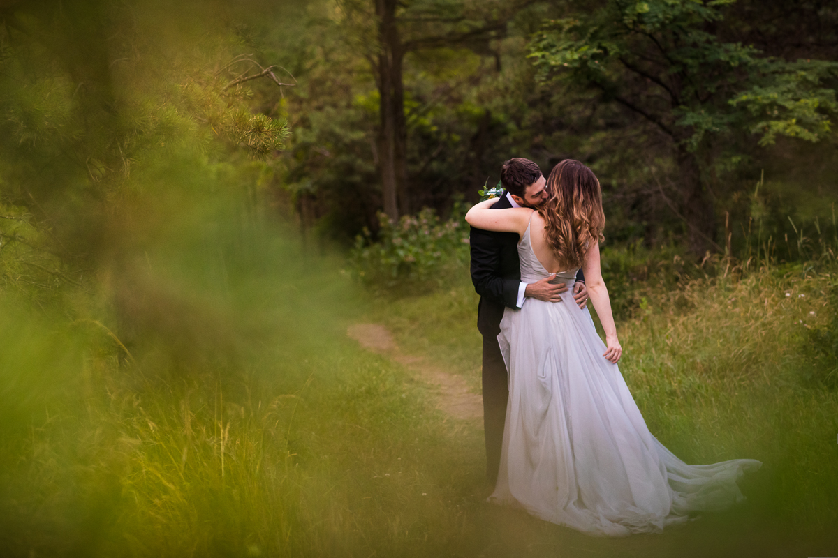 best central pa unique beautiful photographer groom kisses bride on cheek as they hug bride touching silver wedding dress in middle of woods