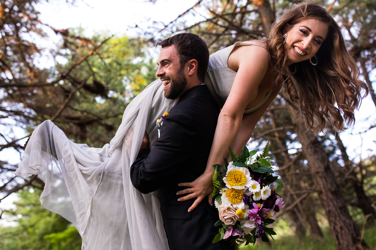 best creative vibrant authentic wedding photographer groom picking up bride holding fake flower bouquet while bride smiles at camera 