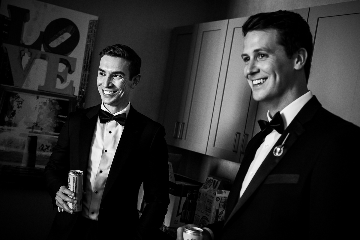 groom and groomsmen standing in kitchen holding beers while getting ready on wedding day