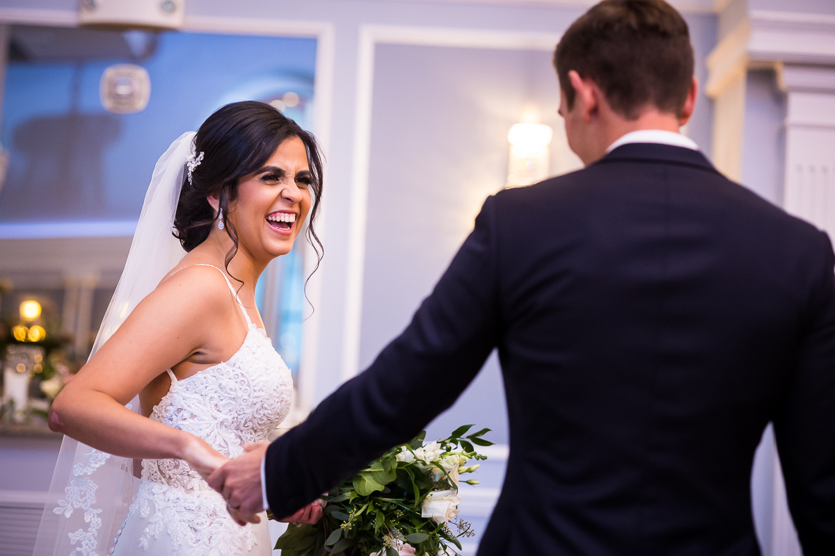 bride smiles as groom holds her hand and looks at her during first look 