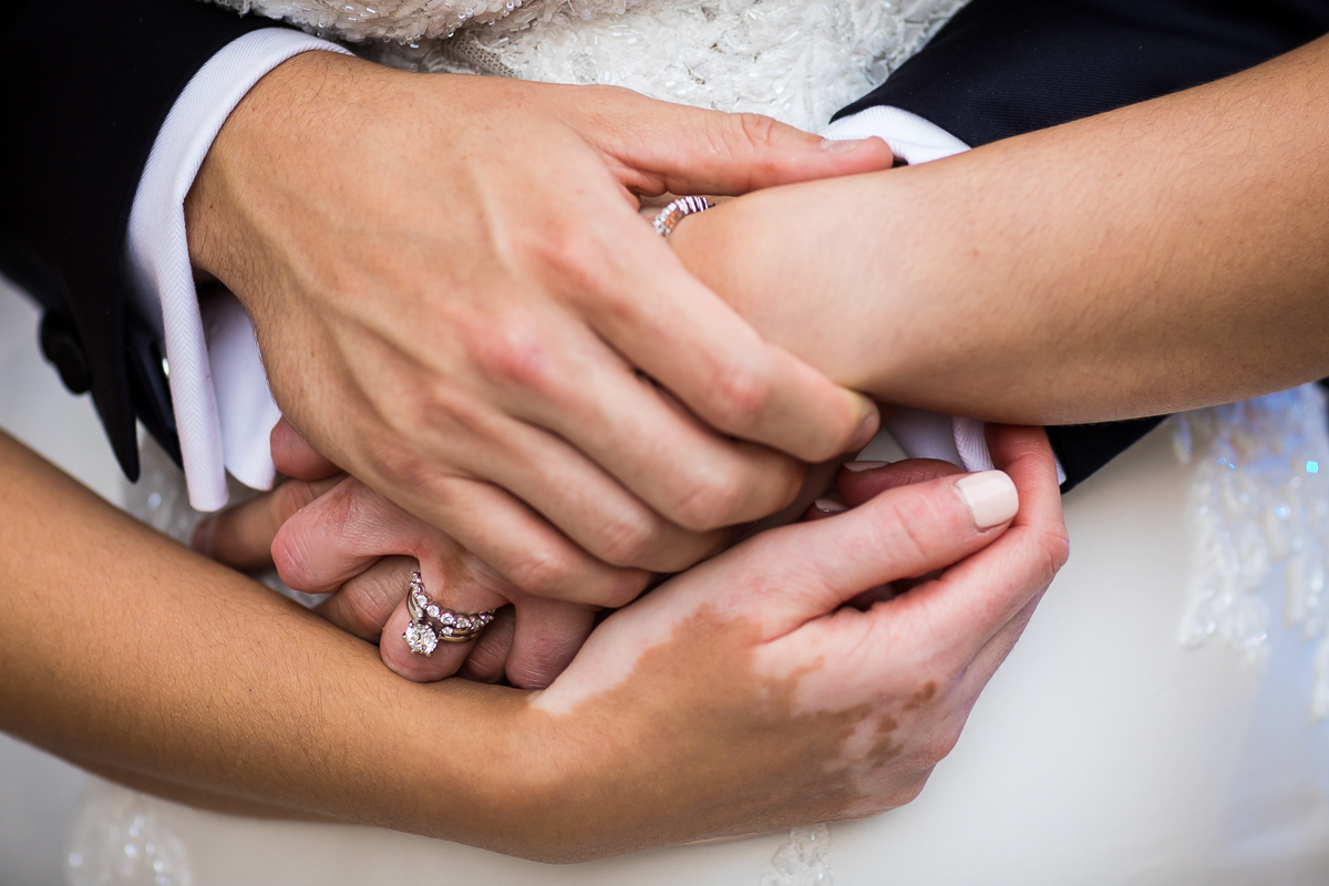 close up photo of bride and groom hands clasped during wedding photos bride wearing round diamond ring with diamond eternity band