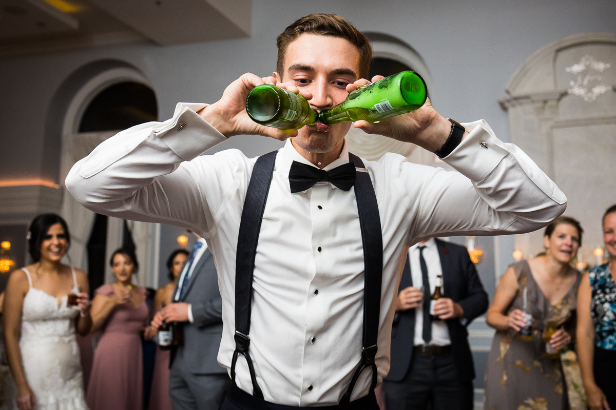 groom drinking two bottles of beer at once during family wedding tradition