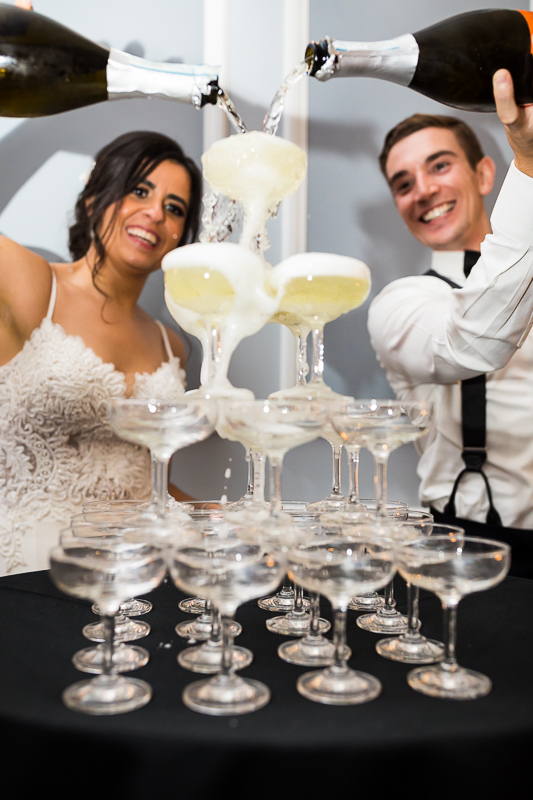 candid fun authentic best wedding photographer bride and groom pour champagne into champagne glass tower