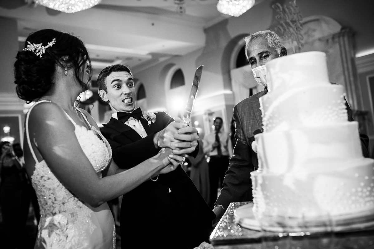 candid fun unique black and white photo groom holding knife with crazy look to cut wedding cake with bride