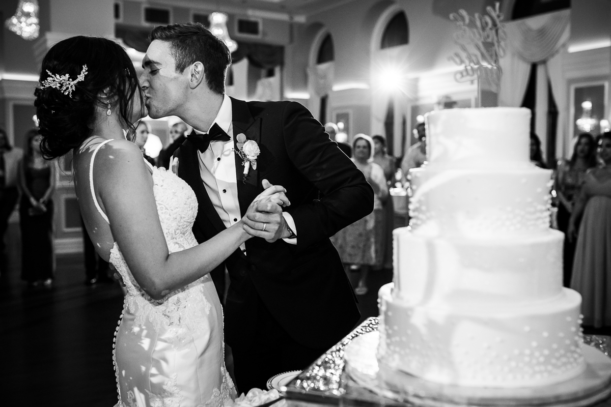 authentic candid Philadelphia wedding photographer black and white photo of bride and groom kissing while cutting cake during reception