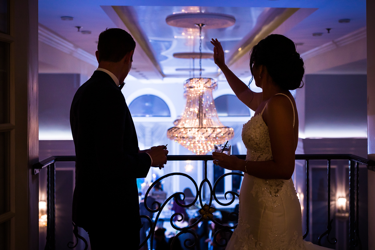best award winning arts ballroom wedding photographer Philadelphia bride and groom waving to their guests from the balcony chandelier in the background