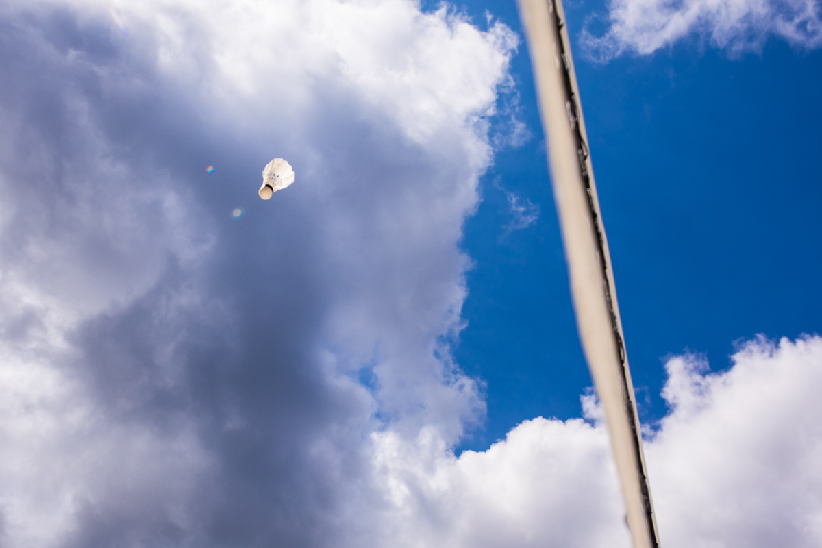 creative artistic DC wedding photographer birdie flying into bright blue sky over net during badminton tournament