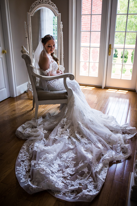 creative artistic wedding photographer historic acres of Hershey bride with long sweeping train sitting in chair posing for traditional bridal portrait in front of mirror and window