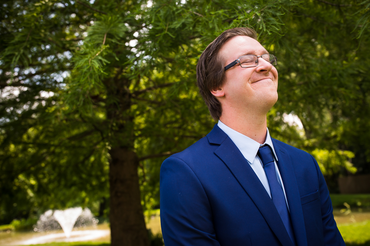 authentic vibrant best central pa wedding photographer groom standing outside with eyes closed before first look with trees and fountains in background