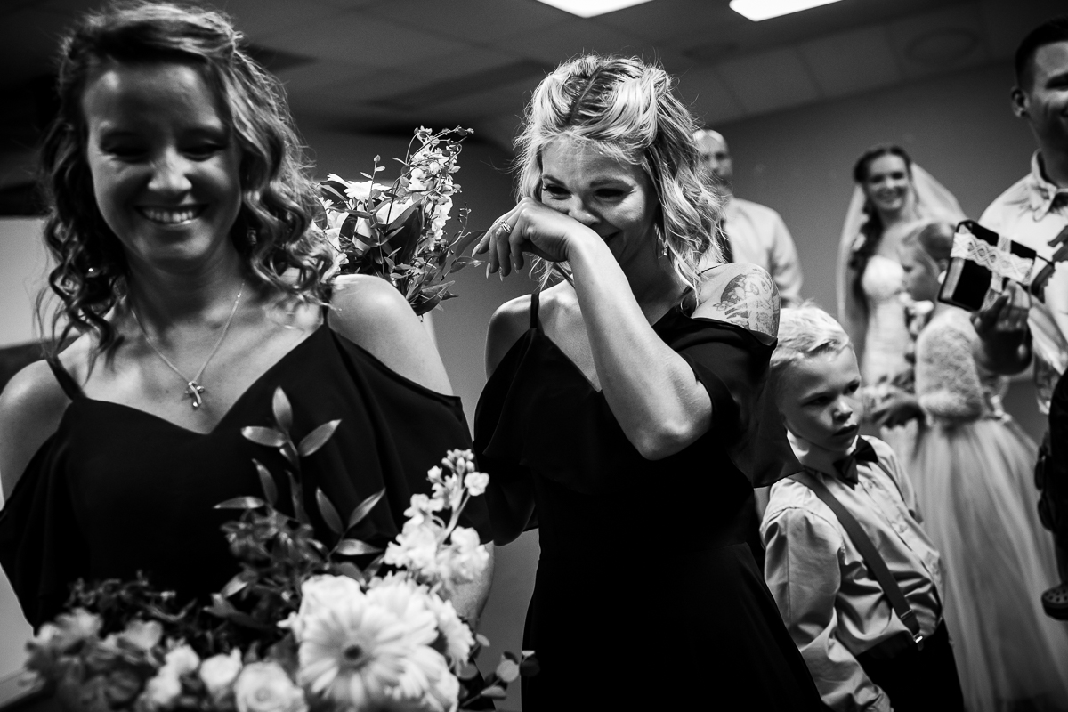 emotional candid black and white photo of bride's sister wiping tears from her face during wedding ceremony