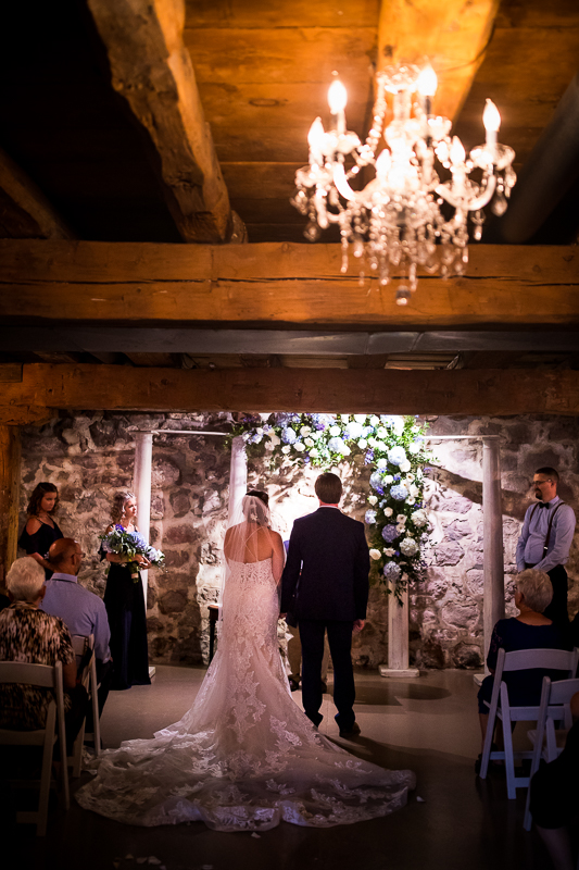 historic acres of Hershey wedding ceremony bride and groom stand in front of officiant during ceremony chandelier hangs above them indoors