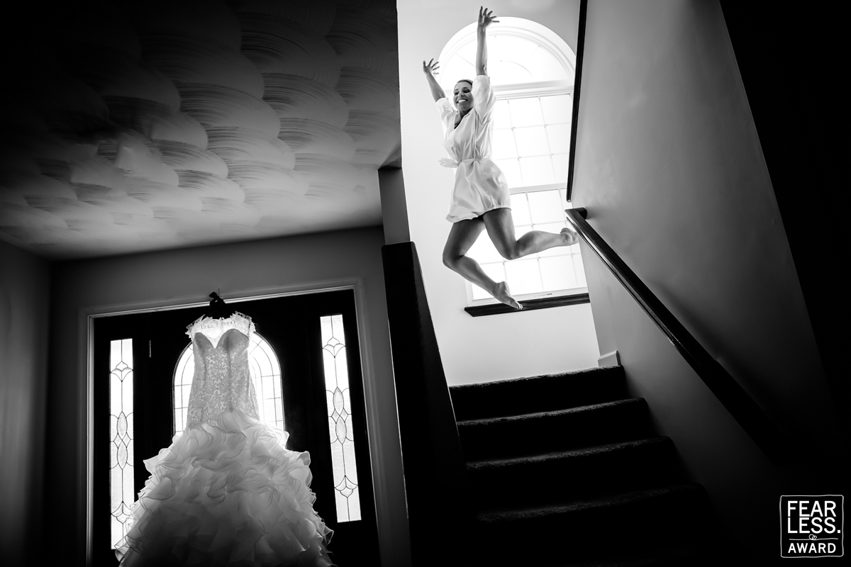 Black and white image of the bride jumping in the air at the top of the steps with her wedding dress hanging in the doorway at the bottom of the steps, best wedding photographers in pa Pennsylvania 