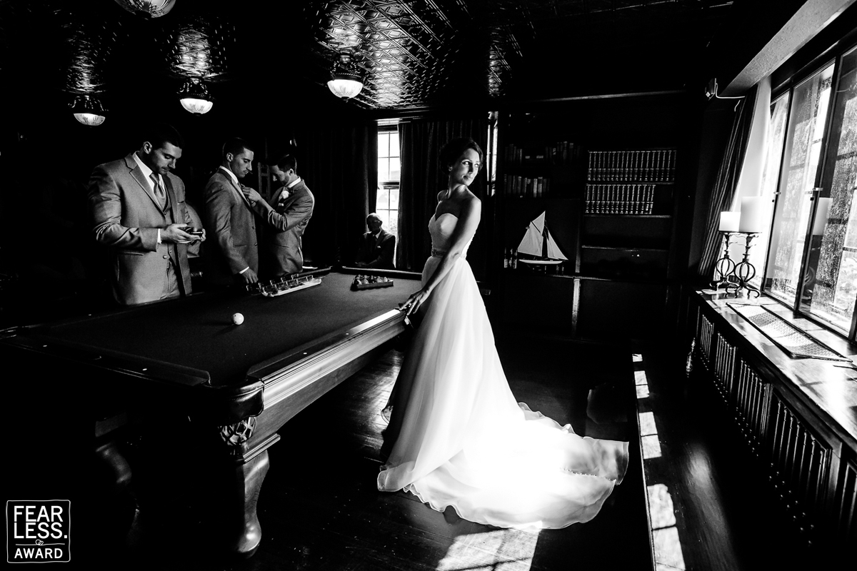 Black and white dramatic image of the bride looking over her shoulder towards a window while standing at a pool table with the groomsmen on the other side best wedding photographers in dc 