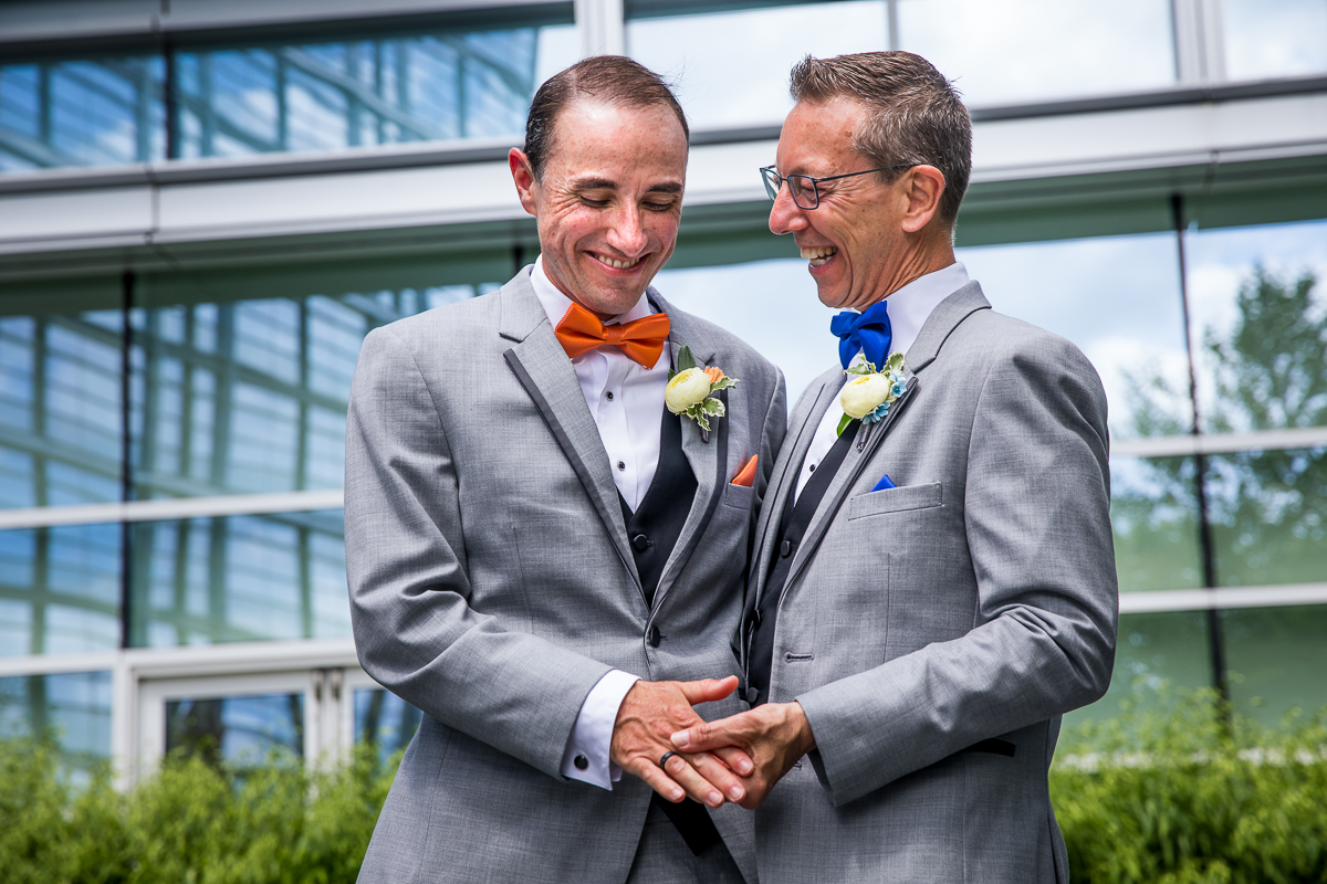 unique colorful authentic wedding photographer DC two grooms one looking at the other smiling while holding hands candid portrait outside Hilton canopy
