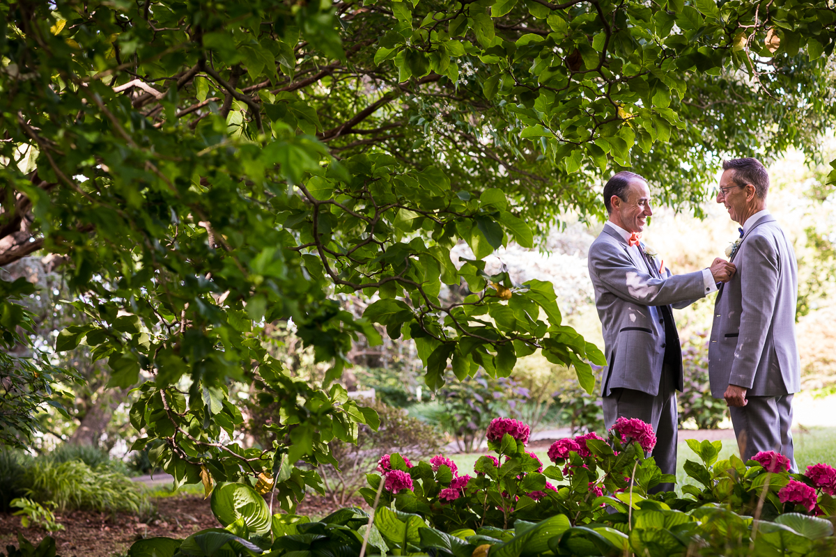national arboretum wedding photographer two grooms standing facing each other while one adjusts pocket square outside gardens during DC wedding portraits candid authentic 