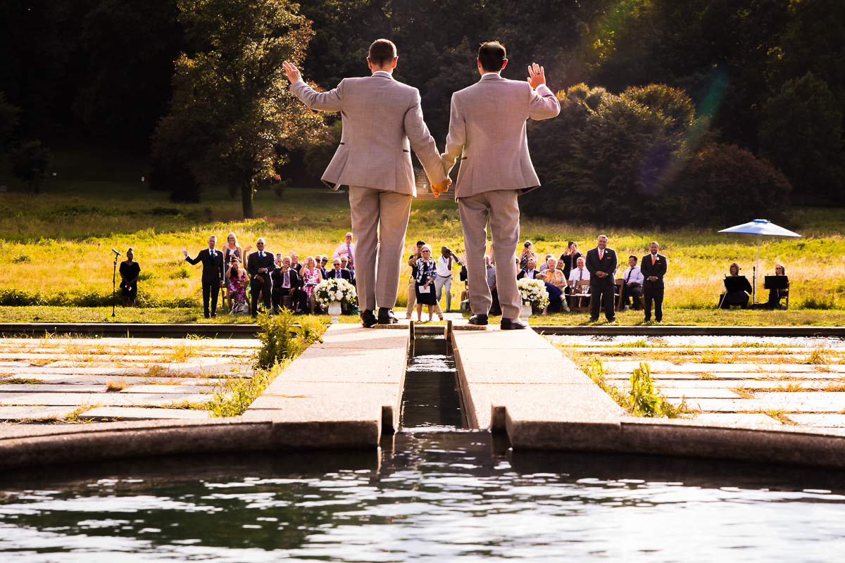 best award winning DC photographer national arboretum wedding two grooms standing by pool waving to guests greeting them before wedding ceremony begins