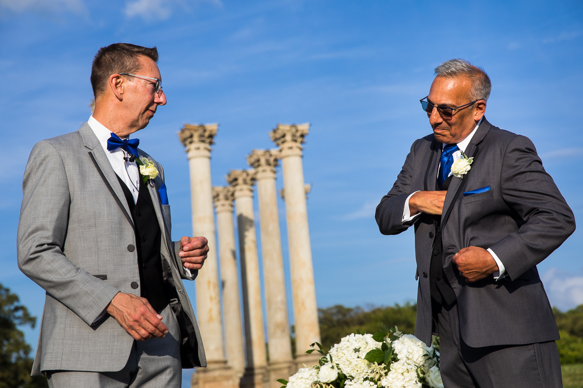 colorful wedding photographer groomsmen gets rings out of pocket during wedding ceremony in front of National Capitol Columns Washington DC