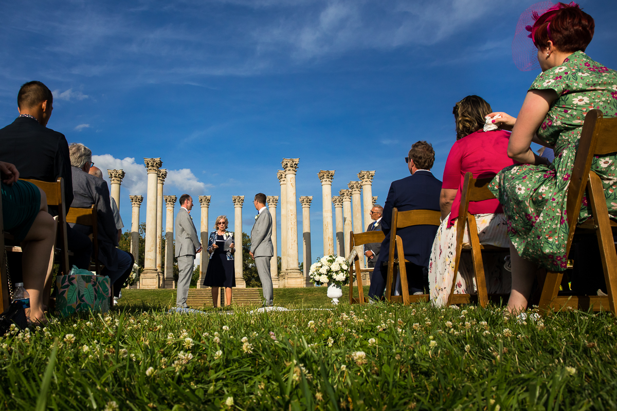 colorful vibrant national arboretum wedding with two grooms standing at altar with officiant National Capitol Columns in background as guests are seated behind them