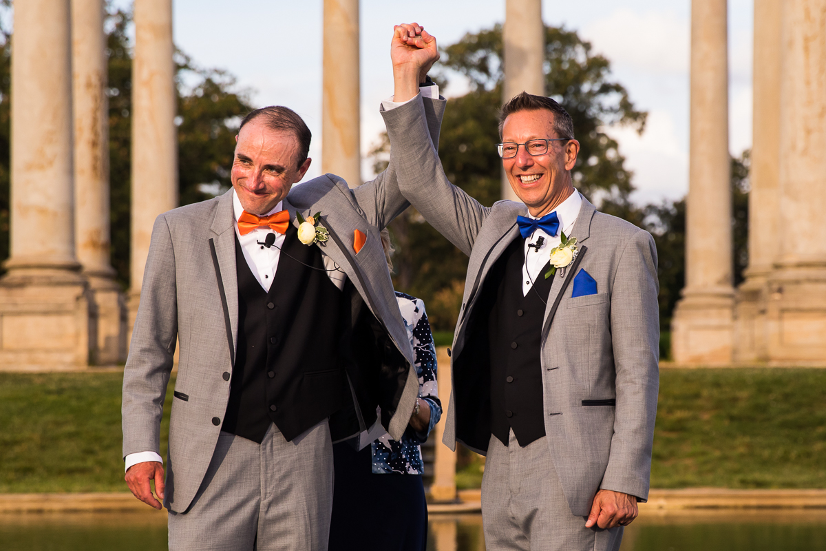 best award winning DC wedding photographer two grooms hold hand at the conclusion of wedding ceremony just married National Capitol Columns national arboretum wedding