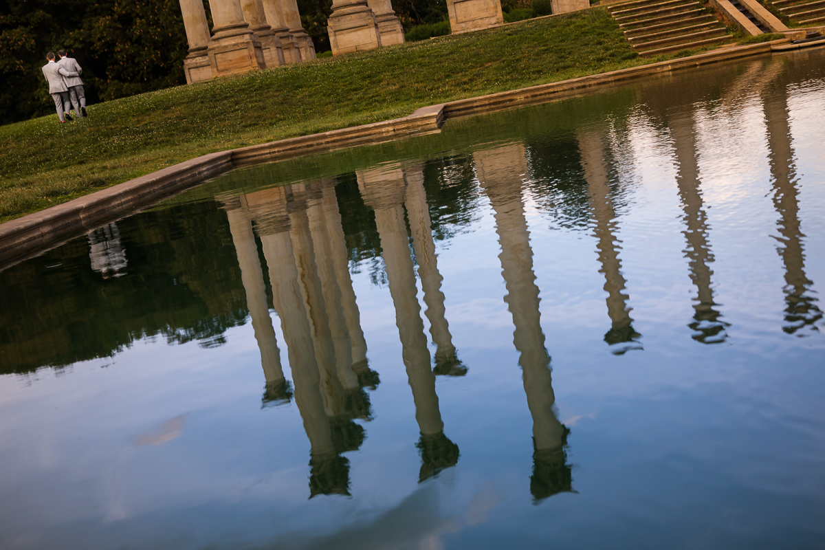 unique artistic wedding photographer two grooms walk in distance with capitol columns reflected in water at national arboretum wedding