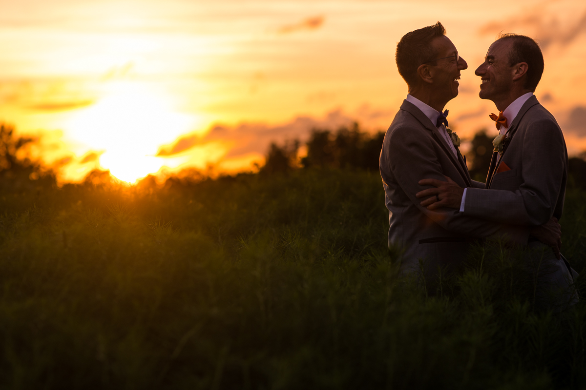 colorful vibrant DC wedding photographer two grooms smile and hold each other during sunset portraits at national arboretum wedding reception
