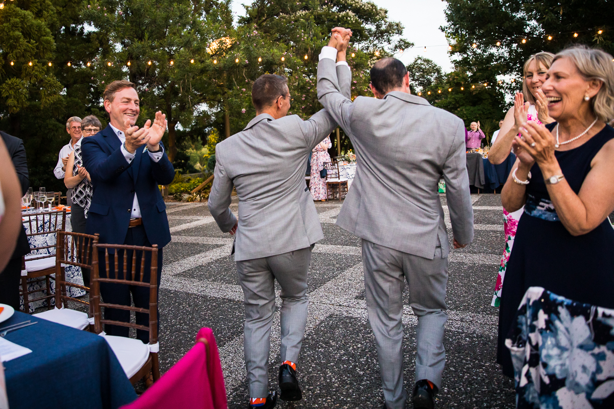 best award winning DC wedding photographer two grooms enter national arboretum wedding reception with guests clapping and cheering as they arrive