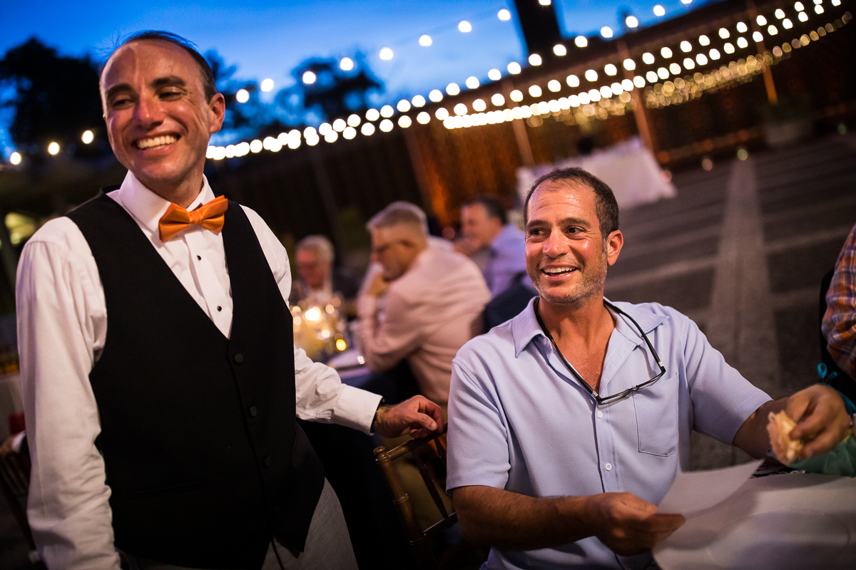 national arboretum wedding reception groom greets guest during dinner at outdoor tables on patio with string lights in background