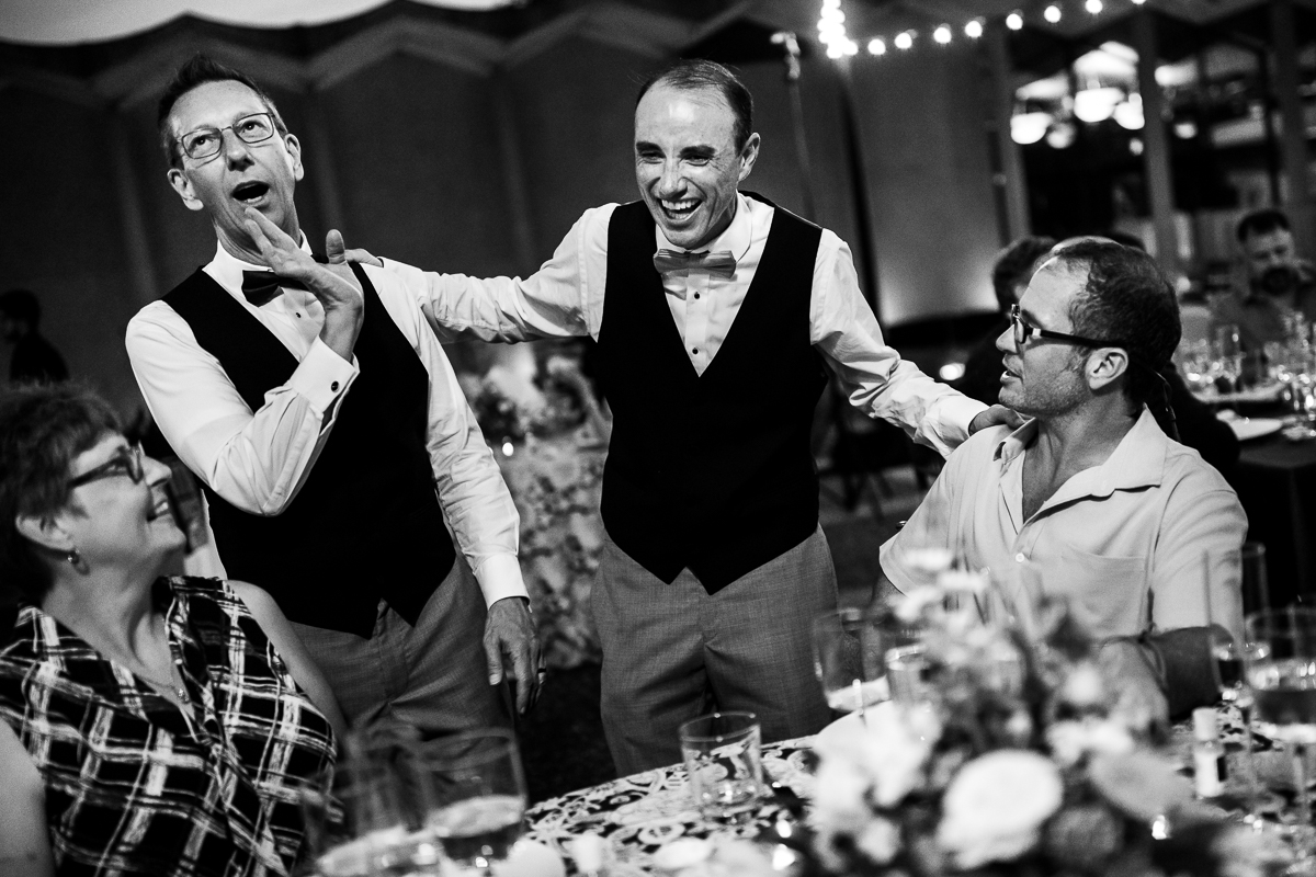 black and white photo of grooms laughing with guests during national arboretum wedding reception on patio joyful happy candid wedding photographer DC