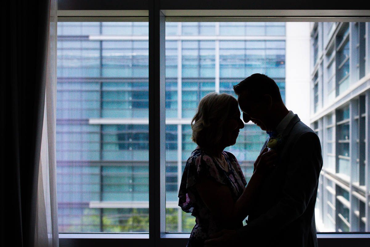 colorful artistic photo of groom with sister silhouetted against window inside dc Canopy Hilton wharf hotel best wedding photographer 