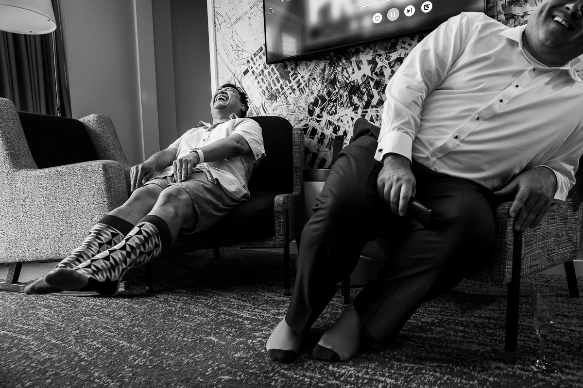 black and white photo of guests laughing while getting ready inside DC Hilton canopy wharf hotel best authentic candid wedding photographer