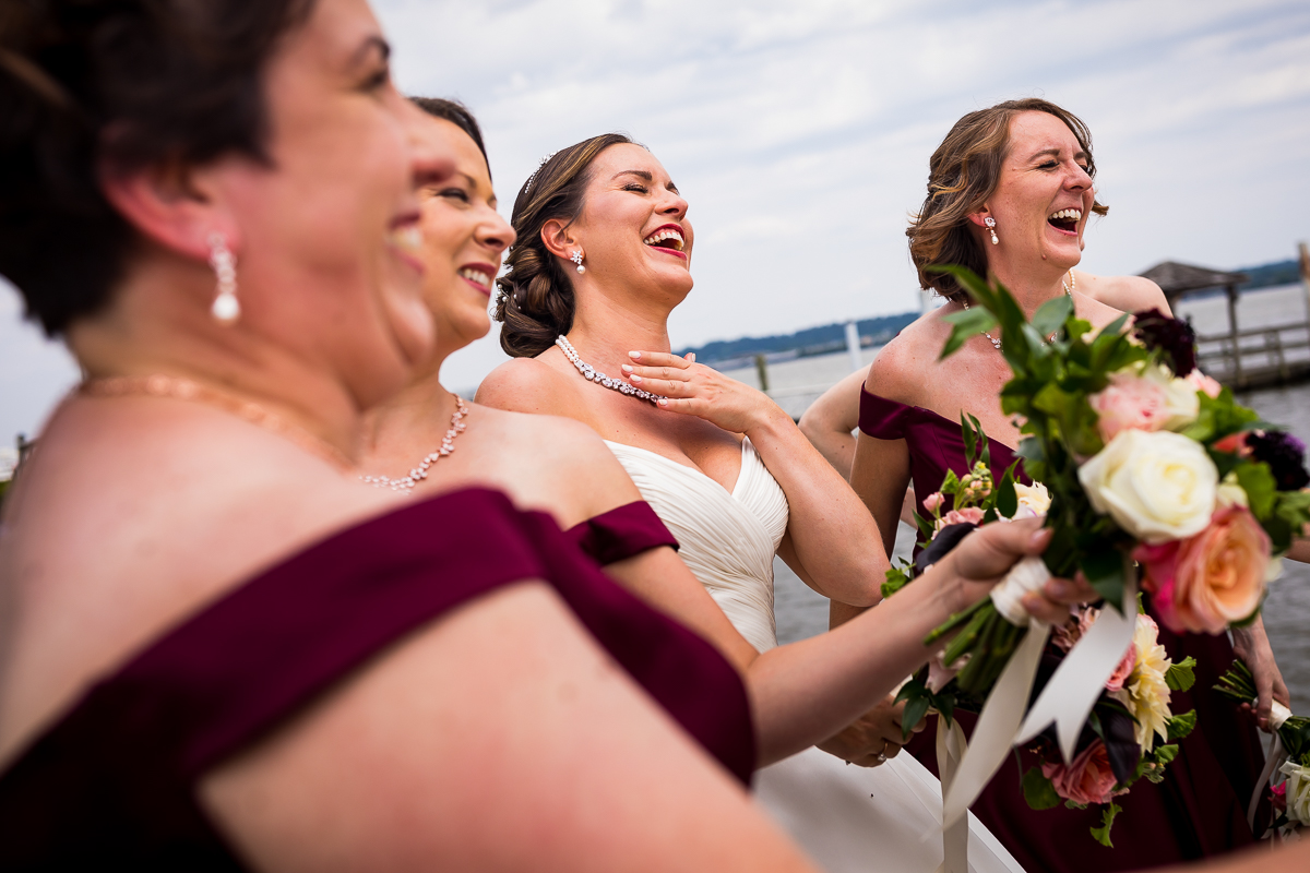 bride and bridesmaids laugh at shipyard park waterfront during wedding portraits candid fun joyful
