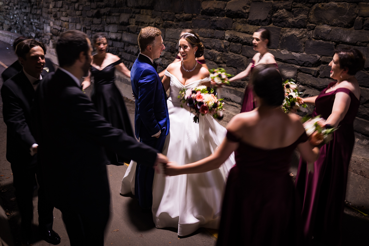 best authentic candid dc wedding photographer Alexandria va bride and groom stand in center surrounding by wedding party singing in Wilkes street tunnel
